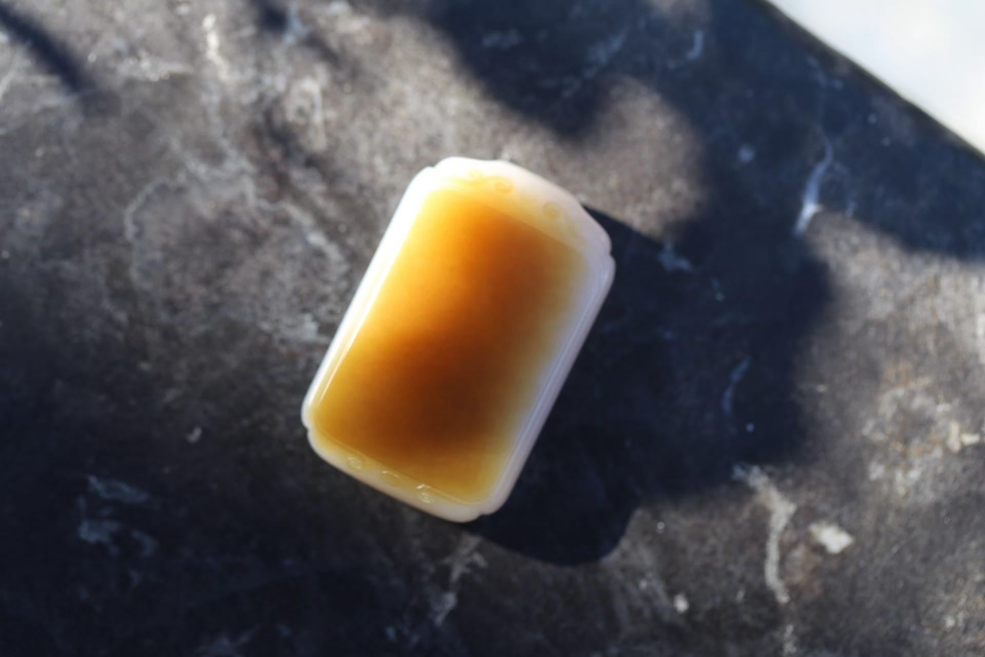 Rectangular plaque with a deep honey-brown face and a white rim, lying on a dark mottled surface in sunlight