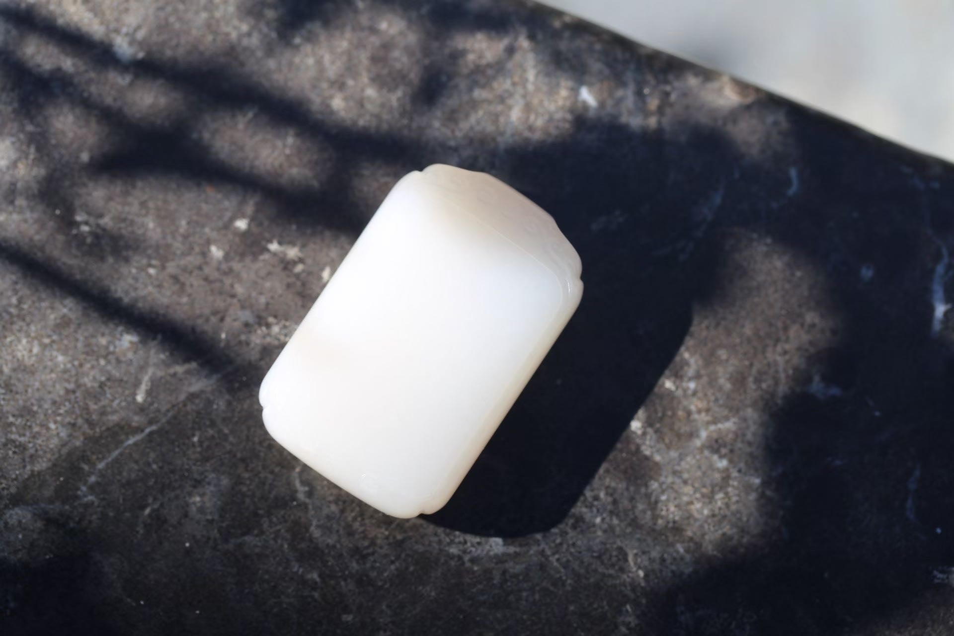 White rectangular plaque with lightly carved ends, lying on a dark mottled surface in sunlight and shadow
