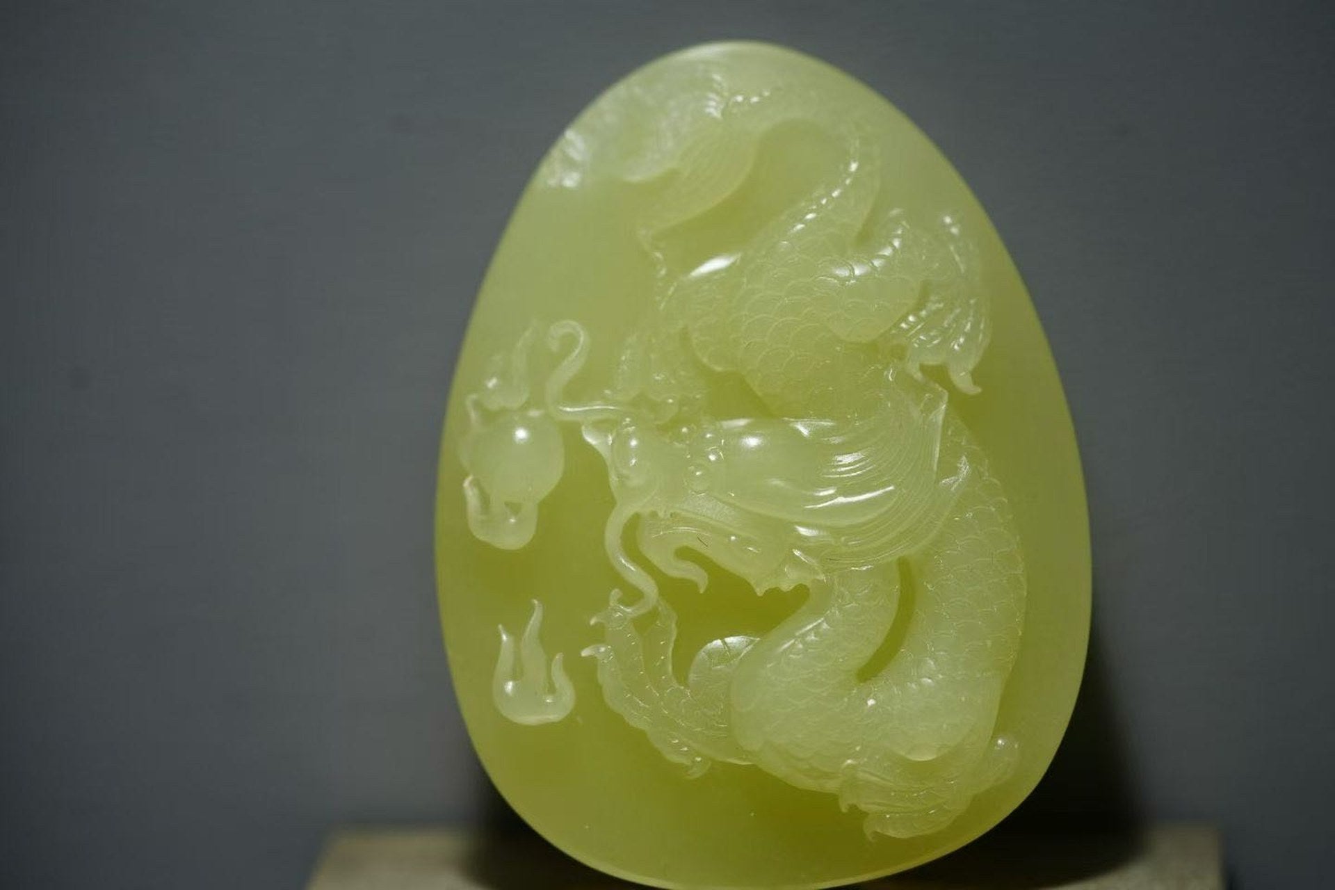 Pale yellow-green oval plaque carved in relief with a coiling dragon reaching toward a flaming orb