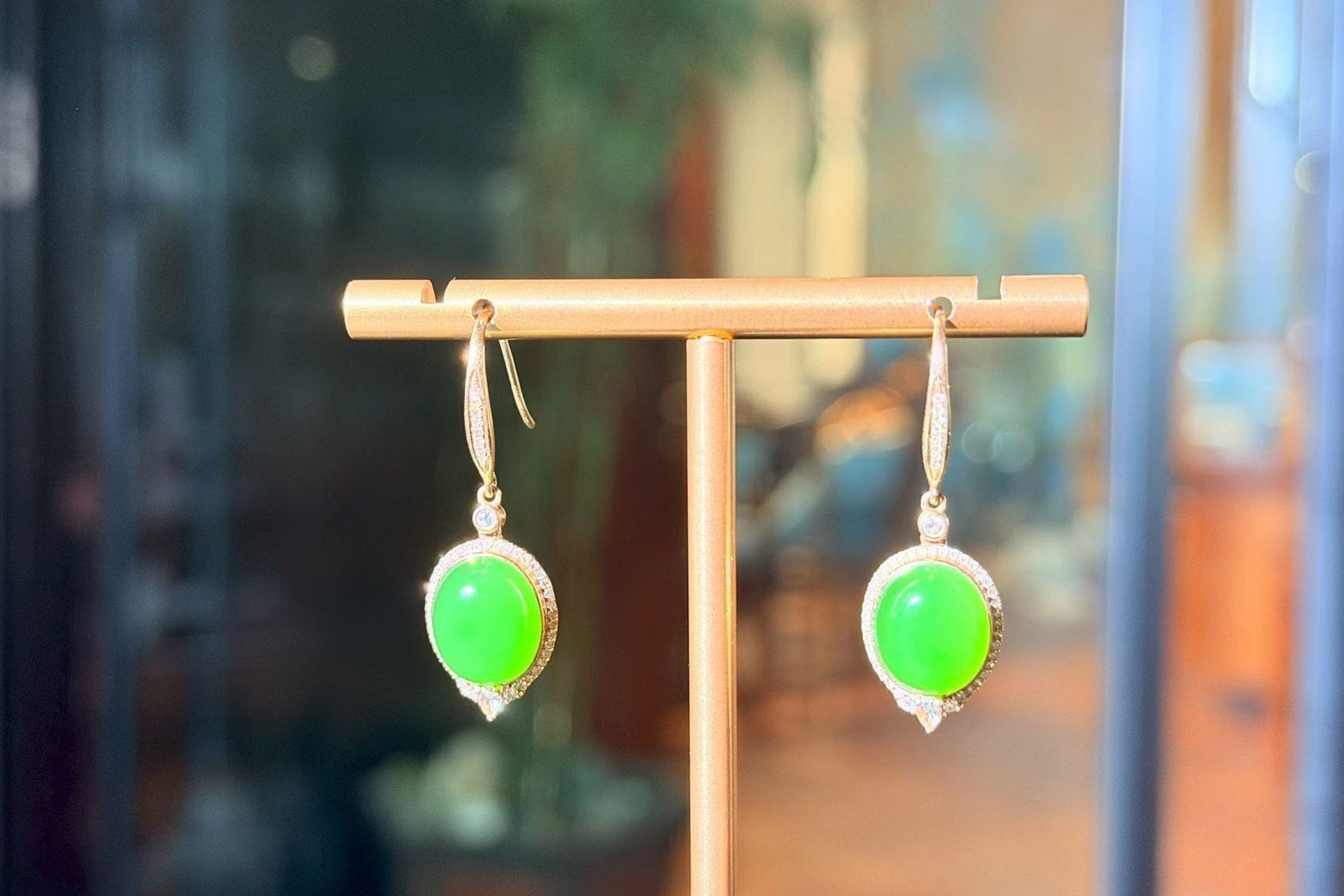 Pair of drop earrings with bright green ovals on gold-coloured hooks, hung on a T-bar stand