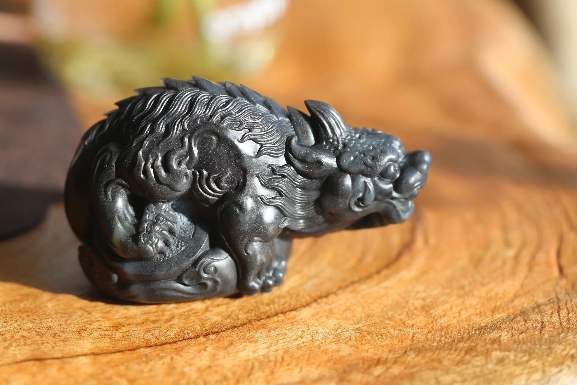 Dark grey carving of a crouching horned beast with a flowing mane, resting on sunlit wood