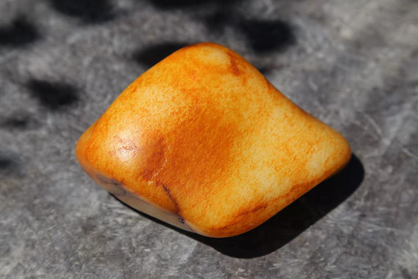 A smooth, rounded stone mottled in honey and orange, resting on a grey surface in bright sunlight