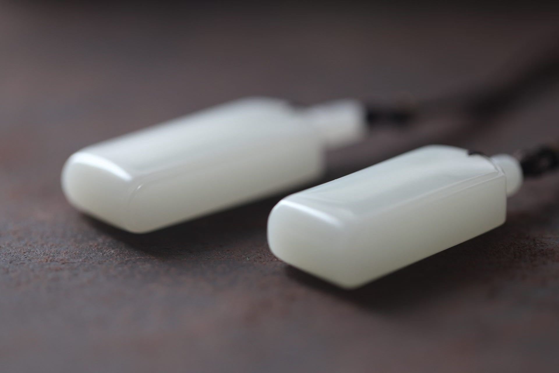 Close-up of two white rectangular pendants with stepped tops, lying on a dark brown surface