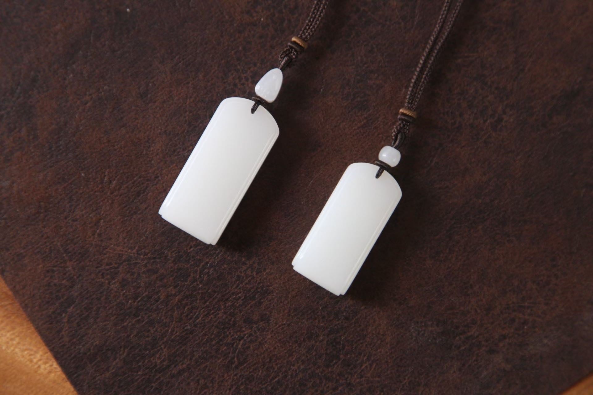 Two white rectangular pendants, each with a small white bead above, lying on dark brown leather