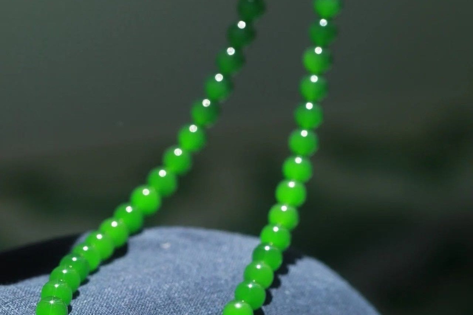 Bright green round beads draped in two lines over blue denim, catching points of sunlight