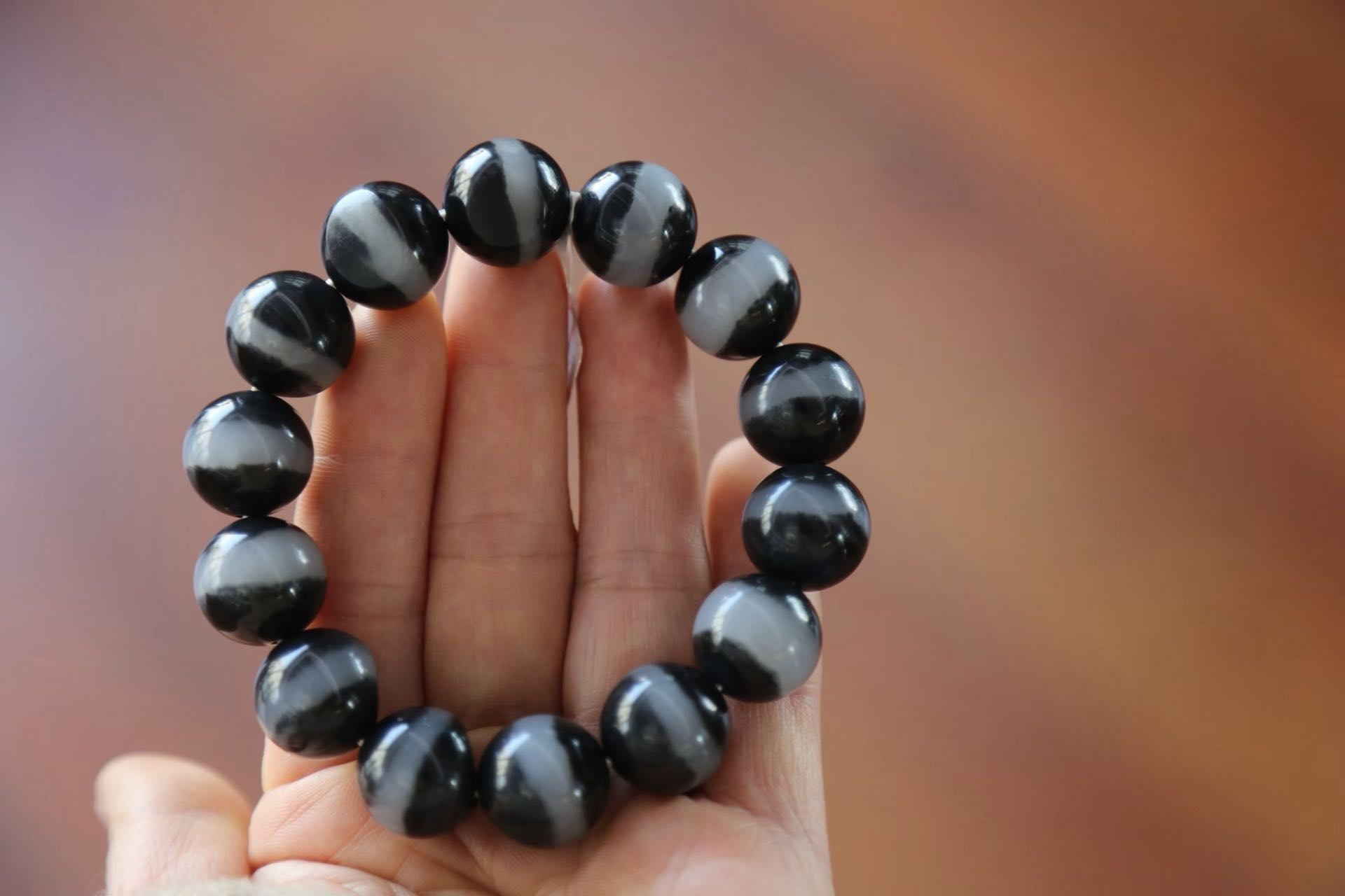 A bracelet of large round black beads, each crossed by a pale grey band, propped upright on an open hand